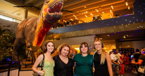 Four woman posing for a picture in front of the Science Center's animatronic Tyrannosaurus Rex.