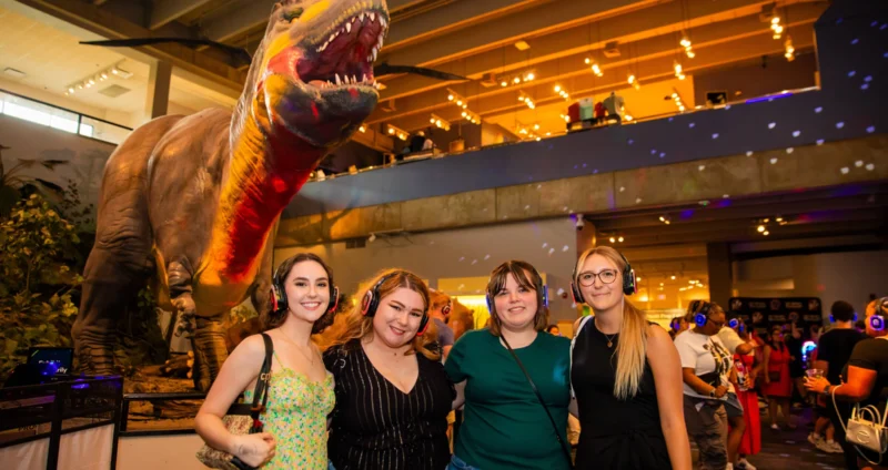 Four woman posing for a picture in front of the Science Center's animatronic Tyrannosaurus Rex.
