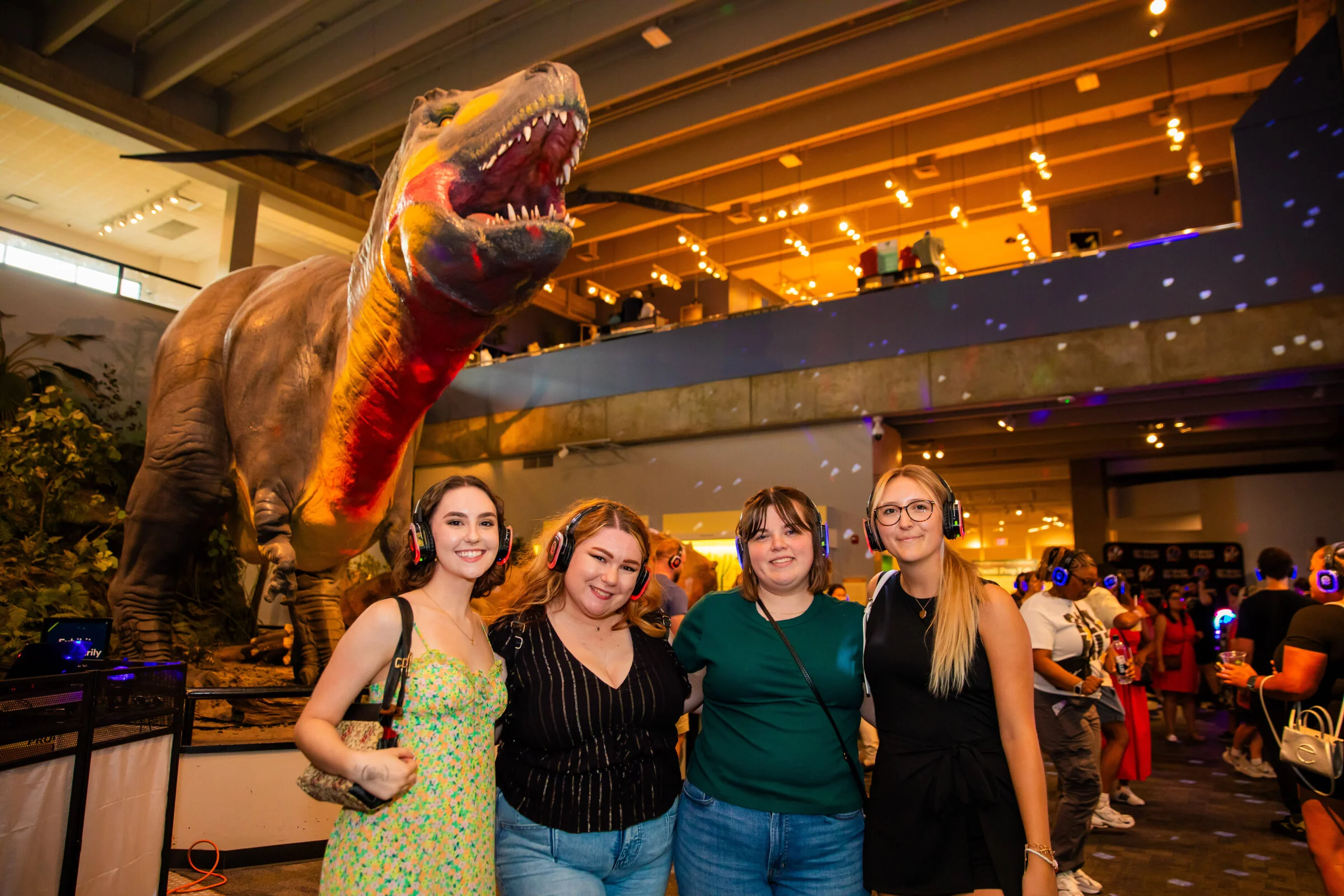 Four woman posing for a picture in front of the Science Center's animatronic Tyrannosaurus Rex.